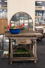 Fototapeta na wymiar Antique Wooden Table with a Drawer and Large Blue Vase with Pink Flowers above it and Mirror Window in the background