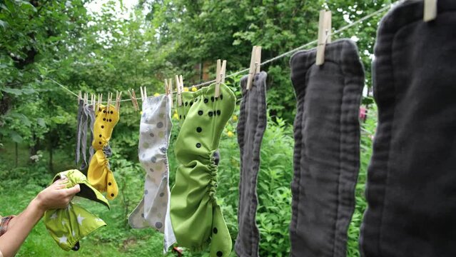 Middle age woman removes reusable diapers to dry on clothesline in garden. Modern eco friendly cloth nappy for infant child hygiene. Sustainable lifestyle, zero waste concept.