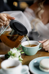 Obraz na płótnie Canvas Woman pouring hot black tea with mint, lemon from teapot into cup, evening tea party