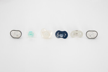 Six different baby pacifiers on a white background. Different types of pacifiers: multiple-piece and one-piece
