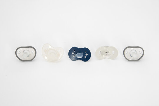 Five Different Baby Pacifiers On A White Background. Different Types Of Pacifiers: Multiple-piece And One-piece