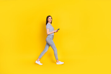 Fototapeta na wymiar Full size profile photo of satisfied lady walking empty space arm hold use modern device gadget isolated on yellow color background
