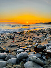 Beautiful sunset on the seashore on a bright sunny day. The waves break beautifully on the pebbles on the shore.Reflection of sunlight on the water surface. Amazing beauty of nature, sunset landscape
