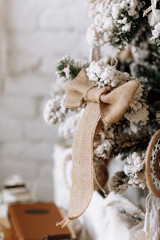 Beautiful Christmas tree decorated with synthetic snow and burlap bow in living room with white brick wall. Merry Christmas, New Year and Happy Holidays background. Eco festive style
