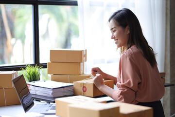 Small startup business concept. Woman tying ropes on a parcel box packs items in preparation for...