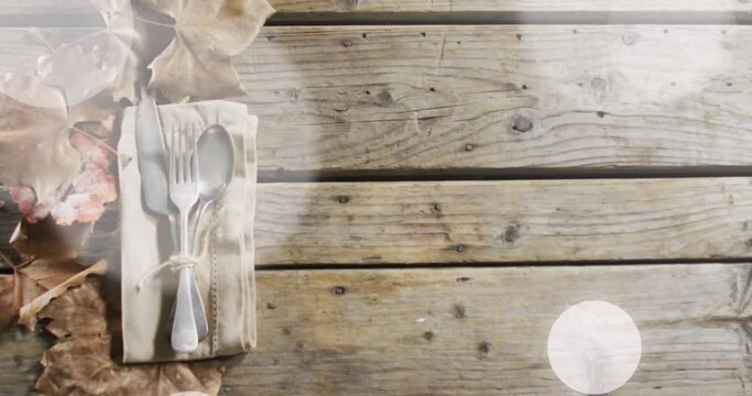 Animation of light spots over cutlery and leaves on wooden background