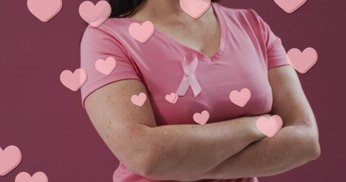 Animation of hearts text over caucasian woman with pink ribbon on pink background