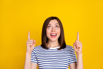 Photo of young attractive cute smiling woman directing fingers up looking empty space unexpected good news isolated on yellow color background