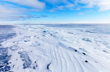 Cold natural background of the snow-covered frozen Baikal Lake on a frosty clear day. Ice hummocks are swept up by dense snow crust. Winter landscape. Extreme tourism