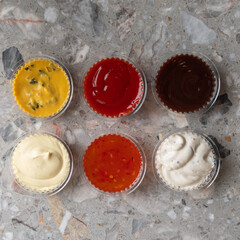 Various sauces and dips in plastic bowls on gray stone background. Copy space