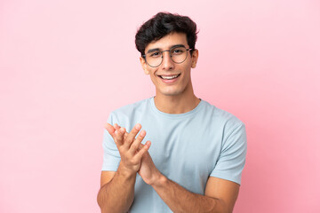 Young Argentinian man isolated on pink background With glasses and applauding