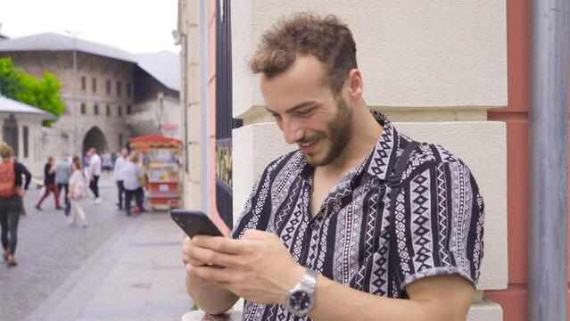 Young man looking at phone outdoors on the street.
Young man looking at his phone at the modern streetside in the city.
