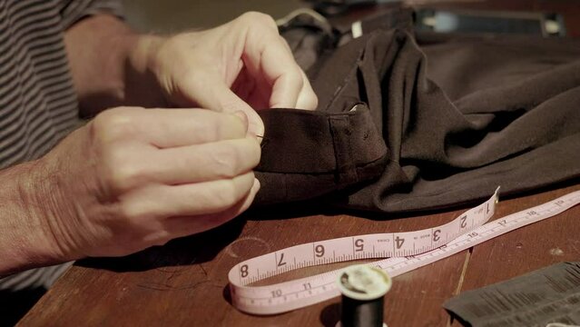 A Man Saving Money By Mending His Own Pants Instead Of Taking Them To The Tailor In These Hard Economic Times.