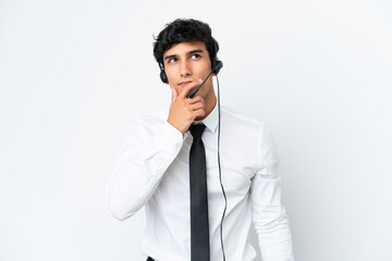 Telemarketer man working with a headset isolated on white background having doubts and with confuse...
