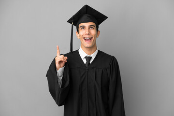 Young Argentinian university graduate isolated on grey background pointing up and surprised