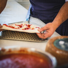 Italian pizza chef preparing and cooking pizza with mozzarella cheese tomato sauce and fresh basil leaf