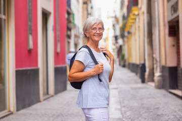 Attractive smiling elderly woman walking in the narrow streets of Seville, Spain, elderly traveler with backpack visiting the old town