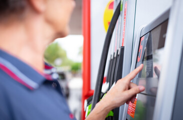 Woman at self-service fuel pump in European gas station types on the display the required amount -...