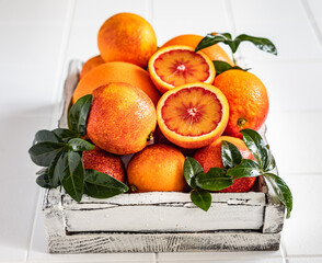 Ripe red Sicilian oranges with leaves in a wooden tray on white tiled background. Blood oranges.