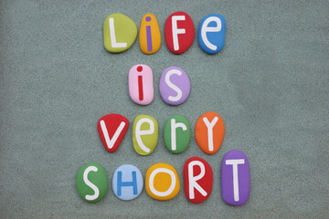 Life is very short, creative message composed with multi colored stone letters over green sand