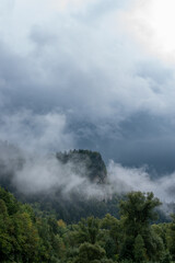 Rocky peak of the mountain covered with forest and surrounded by clouds. Rainy, foggy day in Pieniny National Park, Poland.