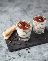 Traditional Italian dessert tiramisu in glass, stone background. Coffee flavored portion dessert made of savoiardi and mascarpone decorated with cocoa.