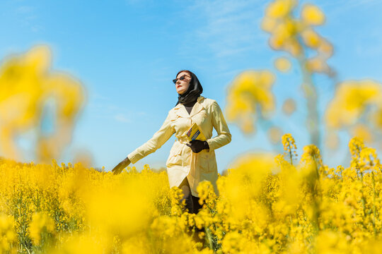 A Young Stylish Woman Poses Among A Blooming Yellow Field Of Rapeseed Under A Bright Spring Sky