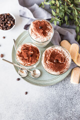 Traditional Italian dessert tiramisu in glass, stone background. Coffee flavored portion dessert made of savoiardi and mascarpone decorated with cocoa.