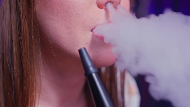 close-up female mouth draws hookah smoke through a pipe and then exhales a large white thick cloud of smoke