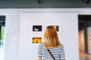 Woman visiting art gallery her looking pictures on wall watching photo frame painting at artwork...