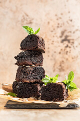 Stack of brownies made of dark chocolate served with cocoa powder and mint on a baking paper, brown...