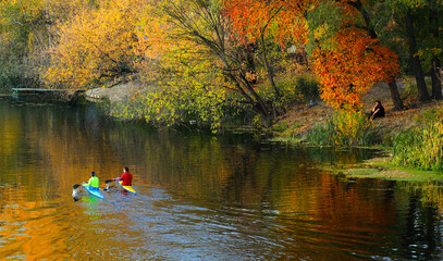 Autumn river with a couple of sports boats kayaks and rowers in colorful T-shirts. Contemplation of the reflection of the sky and autumn foliage in the river water. © Na-um