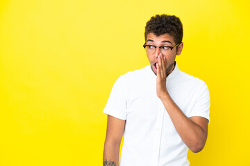Young handsome Brazilian man isolated on yellow background whispering something with surprise gesture while looking to the side