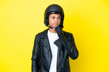 Young Brazilian man with a motorcycle helmet isolated on yellow background having doubts and thinking