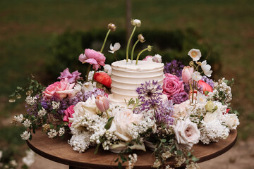 white wedding cake with fresh roses and wild flowers outdoors. Wedding decoration table in the garden, floral arrangement, In the style vintage. Wedding ceremony party