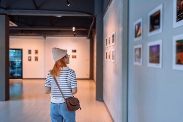 Woman visiting art gallery her looking pictures on wall watching photo frame painting at artwork...