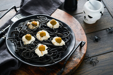 Halloween party Italian black pasta decorated horror  olives like eyes on black plate on old dark...