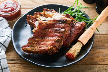 Grilled and smoked pork ribs with barbeque sauce on an old vintage wooden cutting board on old wooden table background. Tasty snack to beer. American food concept. Top view.