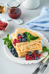 Pancakes. Stack of crepes or thin pancakes with berries, blueberries, red currants, raspberries and honey for breakfast. Homemade breakfast. Copy space. Selective focus.