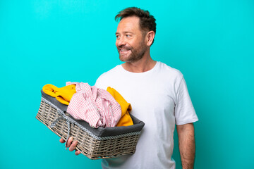 Middle age woman holding a clothes basket isolated on blue background looking side - Powered by Adobe