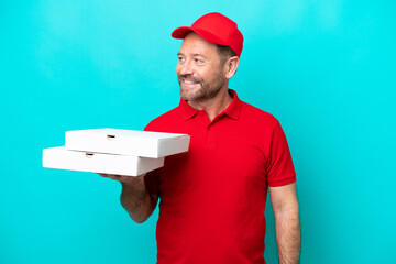 Pizza delivery man with work uniform picking up pizza boxes isolated on blue background looking to...