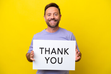Middle age caucasian man isolated on yellow background holding a placard with text THANK YOU with happy expression