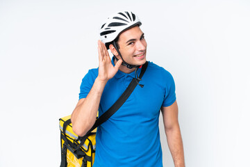 Young caucasian man with thermal backpack isolated on white background listening to something by putting hand on the ear