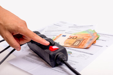 Three-plug extension cord with on-off button, one hand turning off, in the background electricity bills and cash euros. Concept of high energy costs.foreground