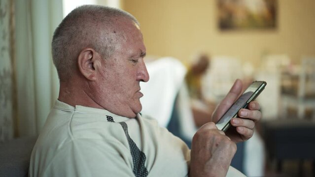 Elderly man with double chin uses smartphone