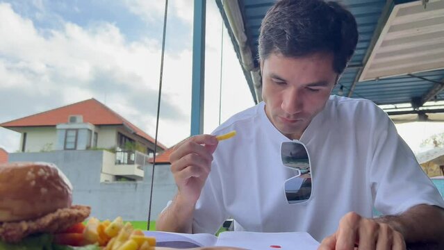 A Clumsy Man Eating French Fries And Drippping Ketchup Sauce On His Notebook. Bad Manners Of Adult Male Person. Ill Manners Of Handsome Asian Guy. Film Grain. Soft Focus. Live Camera. Blur. Candid