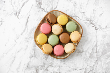 Various colorful macaroons on a plate on a marble table, top view