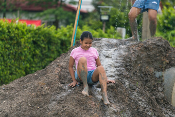 Happy child girl playing in large wet mud and dirt in rainy season