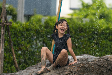 Happy child girl playing in large wet mud and dirt in rainy season