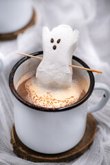 Hot chocolate and marshmallow ghosts served in mugs against a white, spooky background